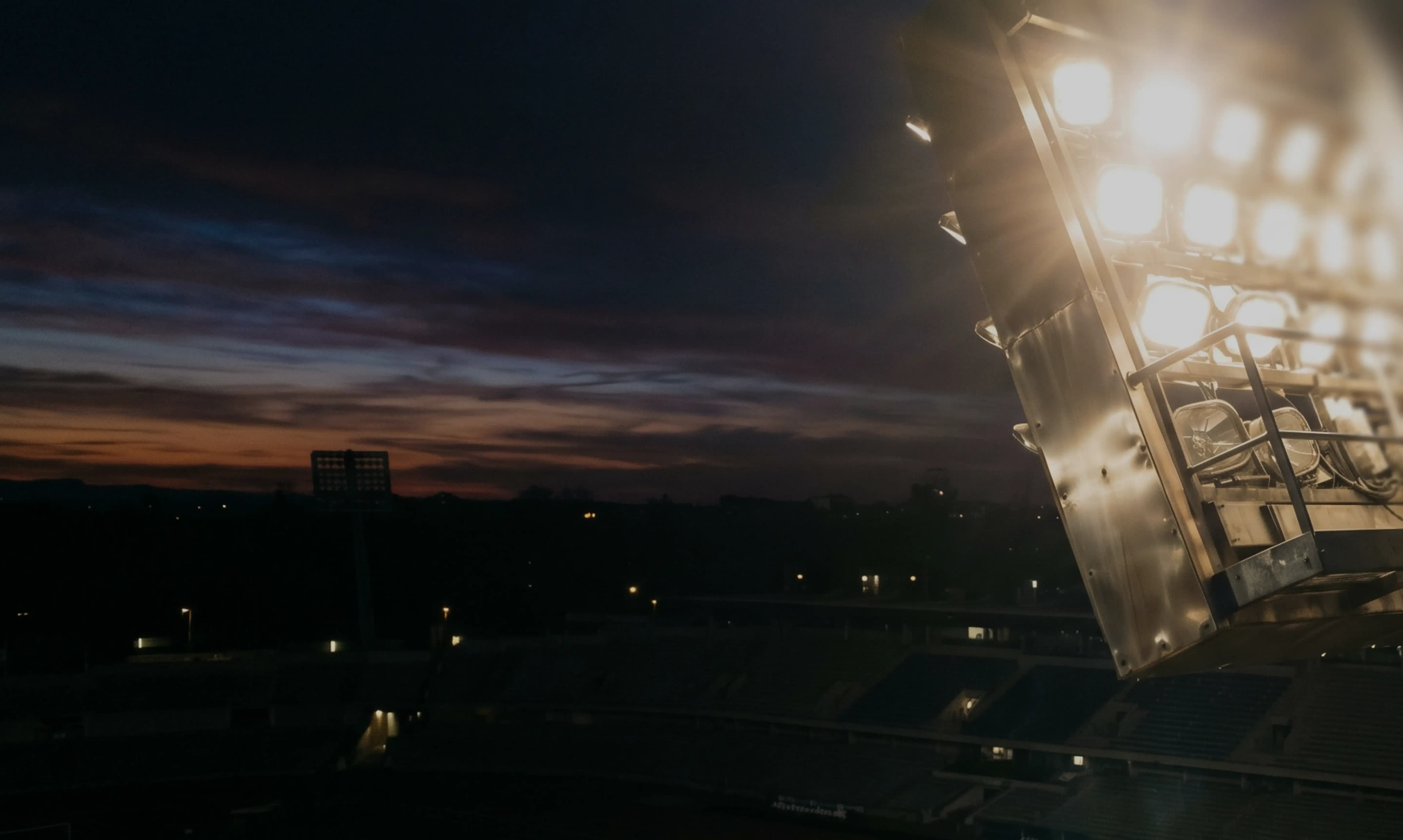 Bright stadium floodlights illuminate a sports field at dusk.